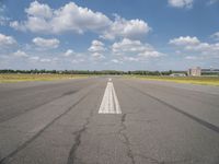 an empty runway surrounded by a field and blue sky with fluffy clouds in the background