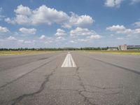 an empty runway surrounded by a field and blue sky with fluffy clouds in the background