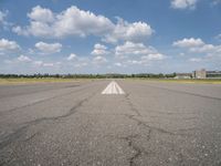 an empty runway surrounded by a field and blue sky with fluffy clouds in the background