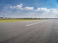 the empty runway at an airport with many planes on it's runways and water tanks in the background