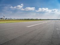 the empty runway at an airport with many planes on it's runways and water tanks in the background