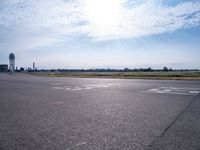 a car drives along an airport road past a water tower and wind vanes, in the sunlight