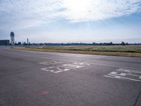 a car drives along an airport road past a water tower and wind vanes, in the sunlight