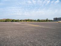 an airport runway with yellow lines painted on it and buildings behind them, in the distance