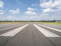 a large airport has many lines in the ground, but few of people are riding bikes down the runway