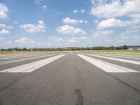 a large airport has many lines in the ground, but few of people are riding bikes down the runway