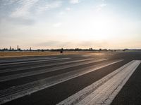 an airport runway with lines painted to look like lines for takeoff passengers at sunset in the background