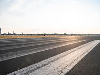 an airport runway with lines painted to look like lines for takeoff passengers at sunset in the background