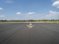 a runway with a yellow arrow painted on the ground in front of an airport and trees in the distance