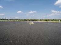 a runway with a yellow arrow painted on the ground in front of an airport and trees in the distance