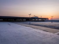 a white and blue walkway leading to a terminal with planes at dusk, with one person on top