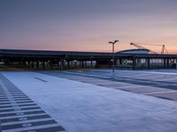 a white and blue walkway leading to a terminal with planes at dusk, with one person on top