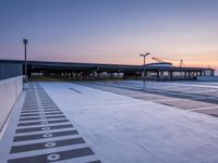 a white and blue walkway leading to a terminal with planes at dusk, with one person on top