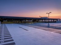 a white and blue walkway leading to a terminal with planes at dusk, with one person on top