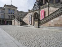 a building has stairs and a clock on it's tower and statues on the sidewalk