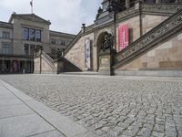 a building has stairs and a clock on it's tower and statues on the sidewalk