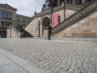 a building has stairs and a clock on it's tower and statues on the sidewalk