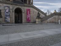 a man rides a bike in the street next to a large stone building and stairs