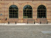 benches with arched windows on an empty brick sidewalk in front of a brick building on the corner