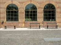 benches with arched windows on an empty brick sidewalk in front of a brick building on the corner