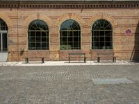 benches with arched windows on an empty brick sidewalk in front of a brick building on the corner