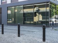 a few poles on the sidewalk by a building with a parking sign in front of it