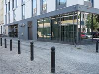 a few poles on the sidewalk by a building with a parking sign in front of it