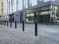 a few poles on the sidewalk by a building with a parking sign in front of it