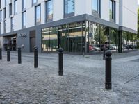 a few poles on the sidewalk by a building with a parking sign in front of it