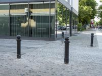 a few poles on the sidewalk by a building with a parking sign in front of it