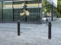 a few poles on the sidewalk by a building with a parking sign in front of it