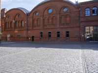 an old bricked building with large windows and arches on it is standing in the center of this square