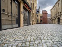 a wide bricked sidewalk that has buildings on each side of it and large windows