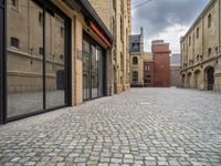 a wide bricked sidewalk that has buildings on each side of it and large windows