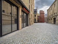 a wide bricked sidewalk that has buildings on each side of it and large windows