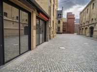 a wide bricked sidewalk that has buildings on each side of it and large windows