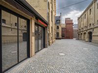 a wide bricked sidewalk that has buildings on each side of it and large windows