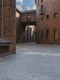 brick buildings are in an empty courtyard area near a bench and building with brick walls