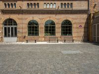 a large brick building with several windows and a bench on the side walk in front