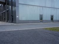 an empty area of a building with metal doors and glass windows, as well as grass and weeds