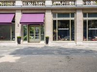 a storefront with purple awning on the windows in front of it, along a brick street