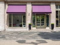 a storefront with purple awning on the windows in front of it, along a brick street