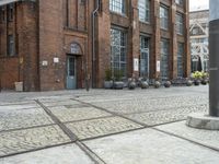 a brick sidewalk with old building and stone planters on either side of it outside