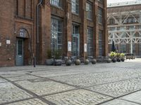 a brick sidewalk with old building and stone planters on either side of it outside