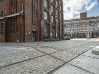 a brick sidewalk with old building and stone planters on either side of it outside