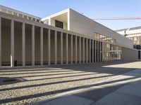 a concrete building on a sunny day with an extended walkway and large white columns, in the foreground