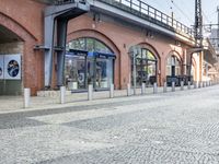 an empty, cobblestone street has a clock and other electrical equipment on the side