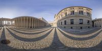 a panoramic view of the exterior of a building, with a walkway and large buildings on either side