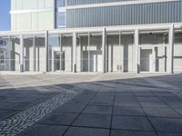 an empty concrete square surrounded by tall glass panels and doors of a modern office building