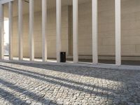 a street in front of a pillar next to some white columns and a black lamp